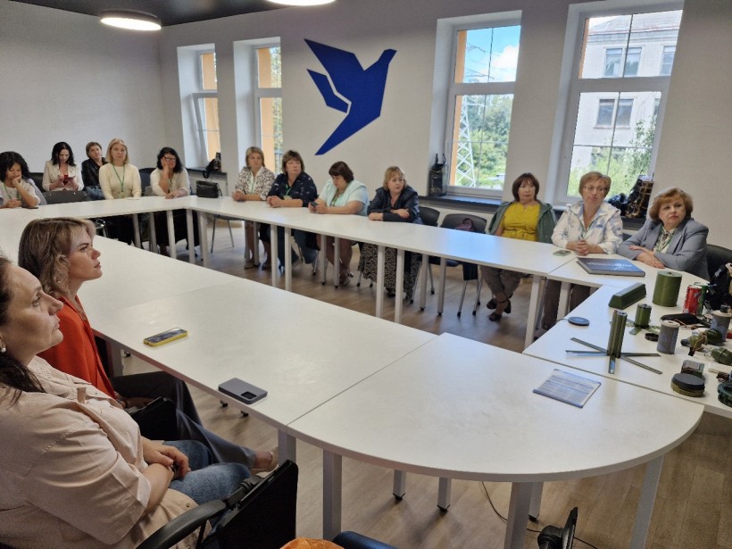 Педагоги сидять за круглим столом під час тренінгу з протимінної безпеки. На столі – макети вибухонебезпечних предметів.