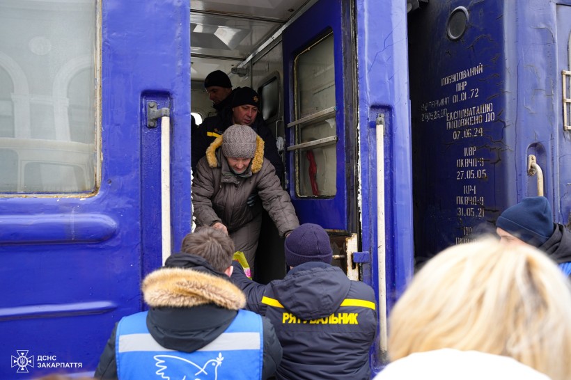 Рятувальник та волонтер Проліски допомагають літній жінці вийти з евакуаційного потяга