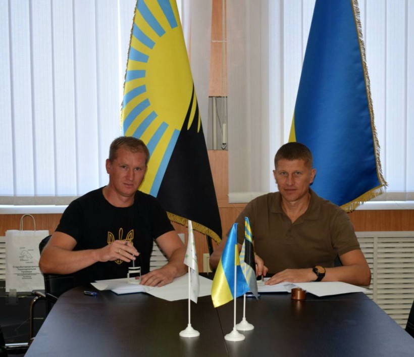 Підписання Меморандуму про співпрацю між Очеретинською селищною і Старобогородчанською сільською територіальними громадами. Голови громад сидять за столом, позаду них прапори Донеччини та України.