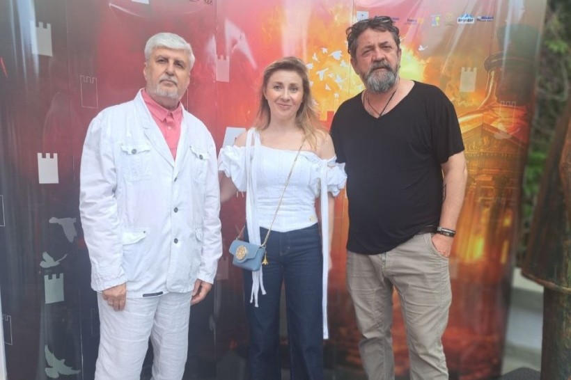 Троє акторів позують для фото на тлі яскравого помаранчево-червоного банер