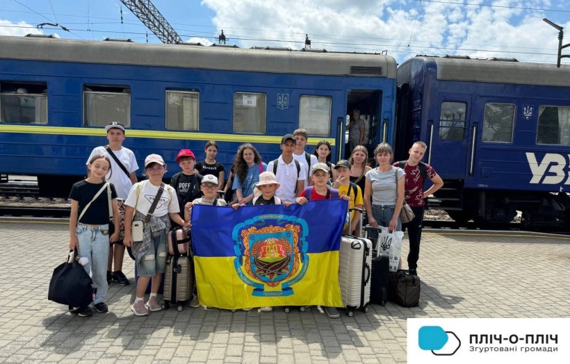 Діти Званівської громади біля потяга на пероні залізничного вокзалу, тримають прапор громади.
