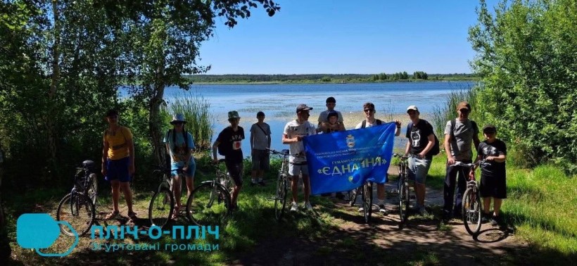 Велосипедисти на березі водойми тримають прапор хабу "Єднання"