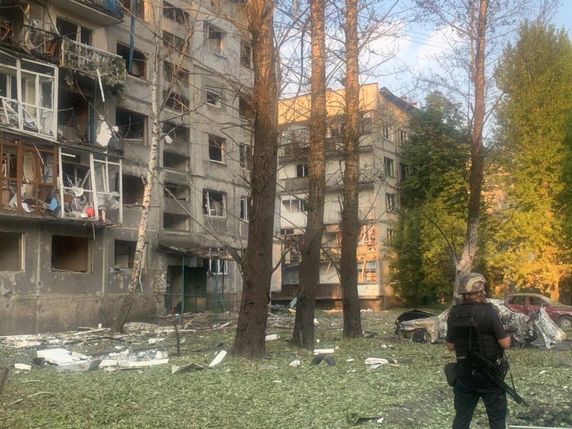 Зруйнований ворожим обстрілом багатоквартирний будинок, поруч з яким стоїть правоохоронець