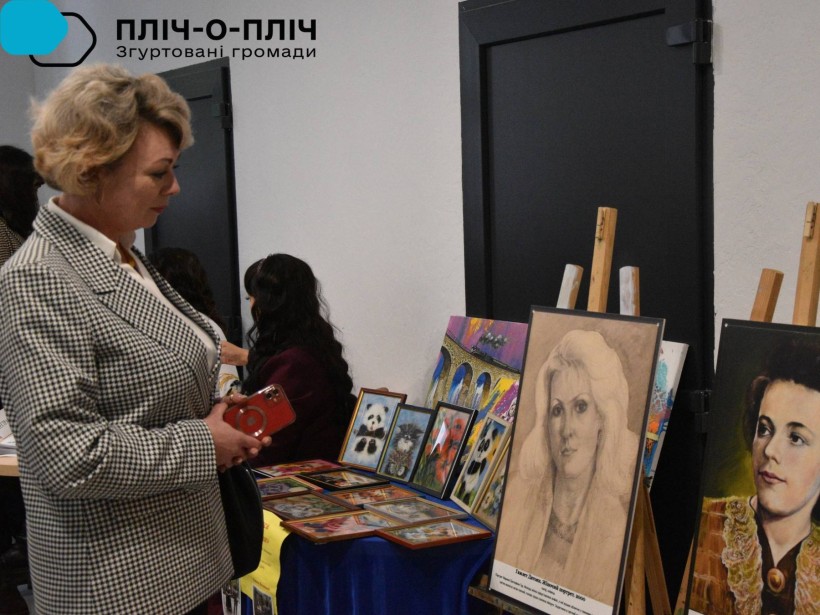 Жінка у діловому сірому костюмі уважно роздивляється портрети.