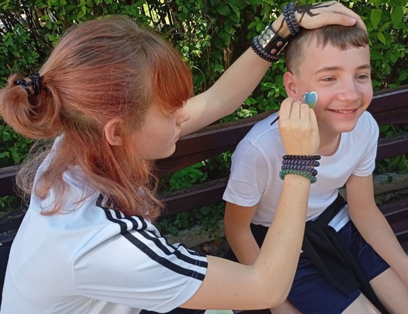 Дівчинка малює хлопчикові на щоці аквагрим у вигляді патріотичного сердечка