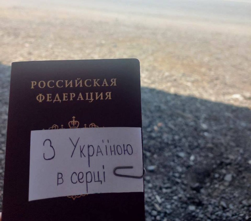 Людина тримає у руках паспорт Росії на якому записка з текстом: "З Україною в серці".