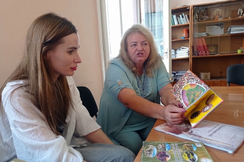 Колега з Франківщини показує відкриту ілюстровану книгу Олександрі Журавель за столом