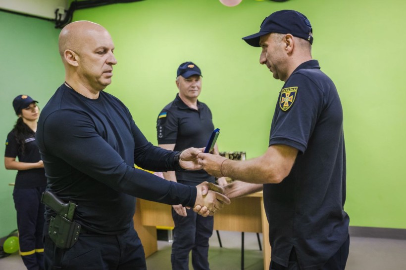 Вадим Філашкін тисне руку рятувальнику та вручає йому нагороду.