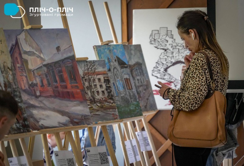 Шанувальниця творчості художниці уважно з захопленням вдивляється у пейзажі міста на картинах.