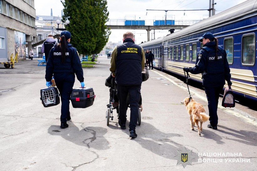 Рятувальник та полійейські везуть людину на кріслі колісному, яка приїхала евакуаційним потягом