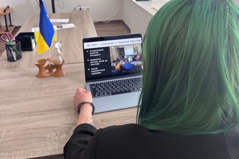 Вигляд з-за плеча пані Антоніни, яка працює за ноутбуком, на екрані відкрито презентацію з заголовком «Кейс: співпраця з Червоним Хрестом»