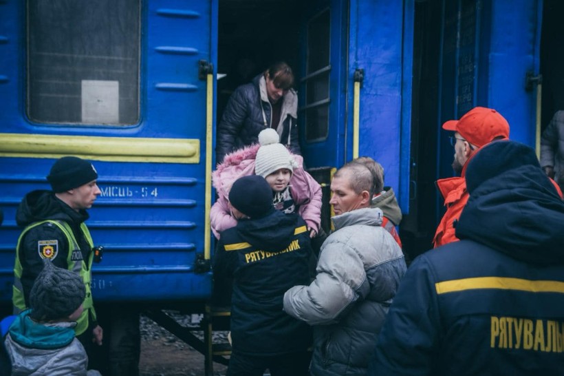 Рятувальники допомагають дитині вийти з евакуаційного потяга, слідом спускається мама