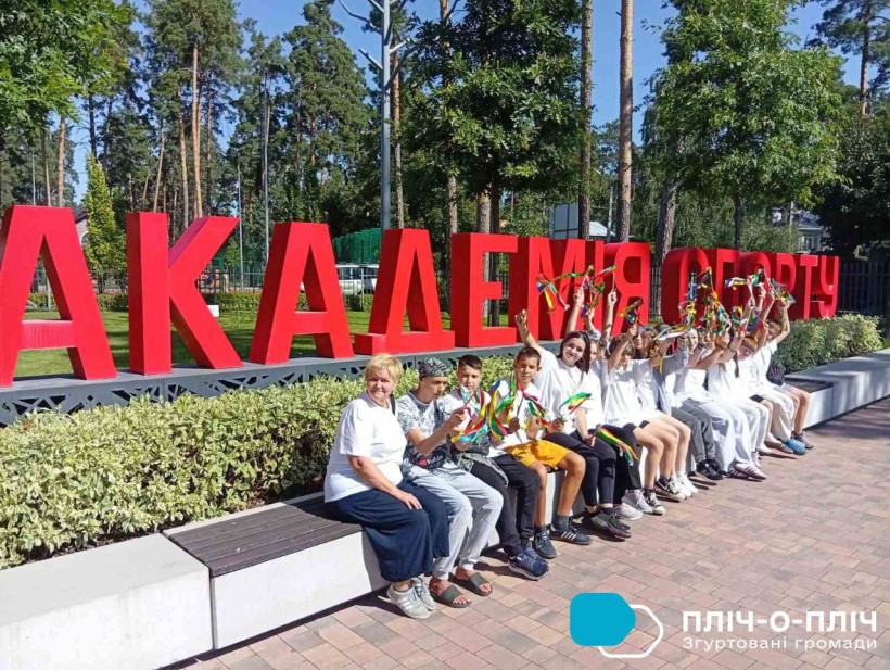 Діти сидять на лавці біля літер "Академія спорту"
