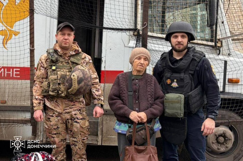 Літня жінка поруч з рятувальниками з евакуаційної групи Фенікс, позаду евакуаційний автомобіль