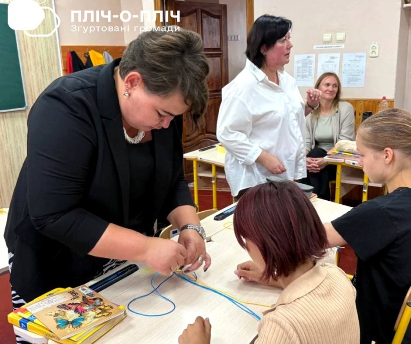 Вчитель допомагає дівчинці робити браслети з жовто- блакитних ниток.