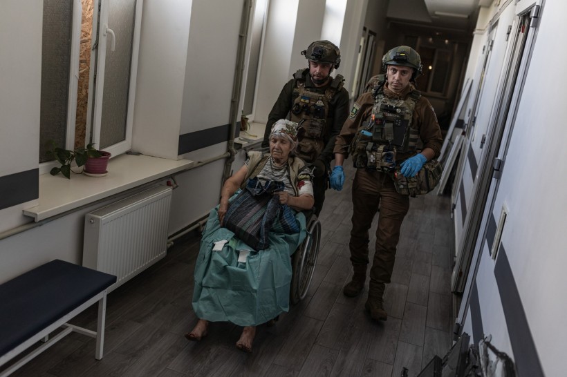Парамедики везуть літню жінку на кріслі колісному у приміщенні закладу