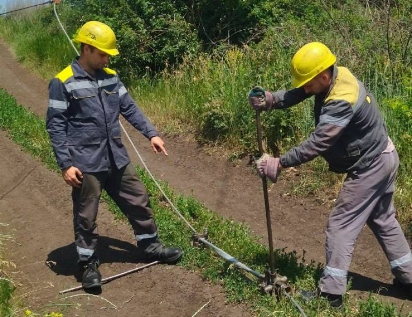 Два співробітника ДТЕК з інструментами лагодять електромережу.