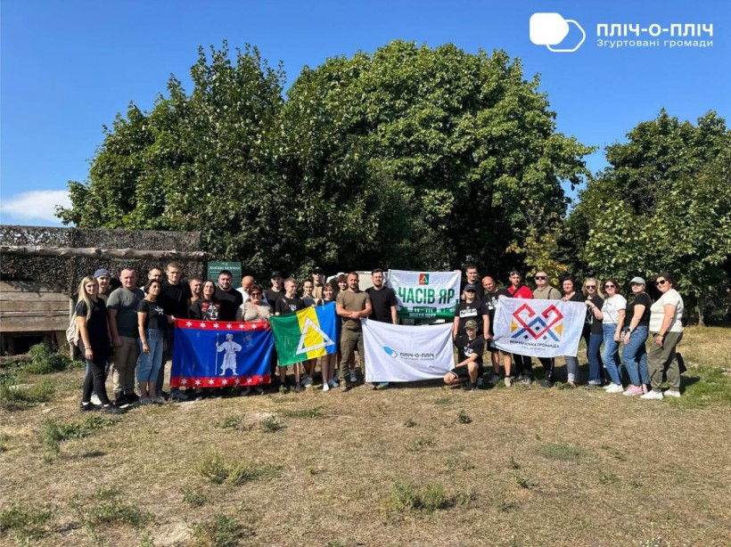 Спільне фото. Чоловіки та жінки стоять на вулиці, тримають прапори громади та спонсорів .