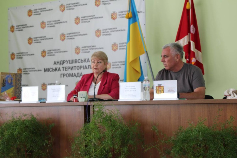Білецька Галина голова Андрушівської громади та начальник Миколаївської міської військової адміністрації Володимир Проскунін. Сидять за столами та обговорюють розвиток та підтримку громад.
