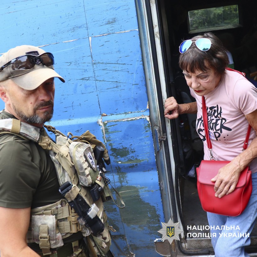 Жінка виходить з евакомобіля, поруч стоїть поліцейський