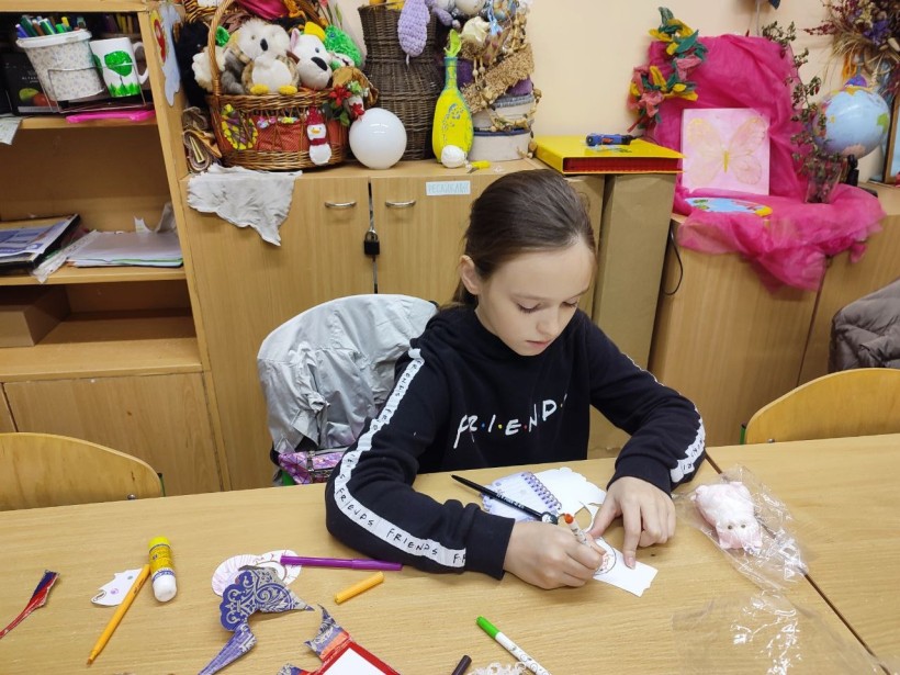 Дівчина за столом займається виготовленням поробки