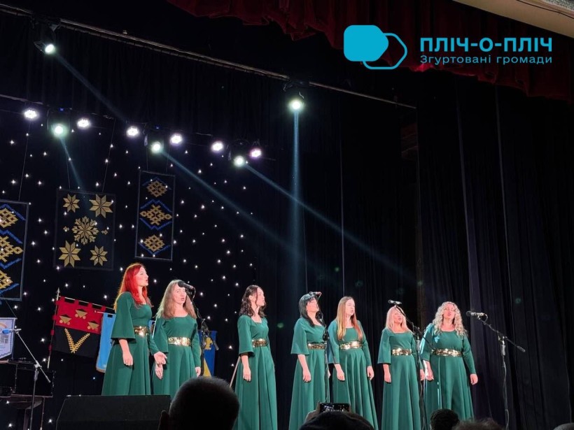 Жіночий ансамбль народної творчості. Жінки у зелених платтях співають на сцені.