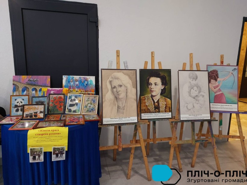 Виставка. На мольбертах стоять портети жінок поруч малюнки