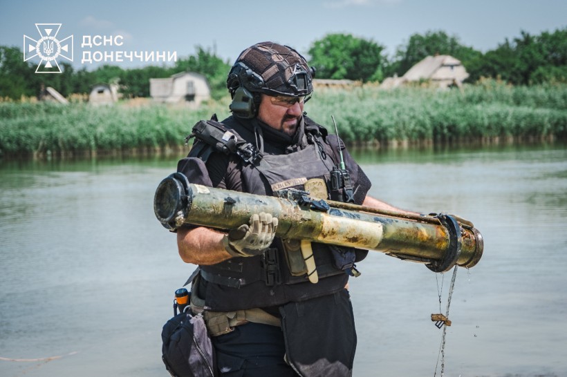 Фахівець розмінування у повній екіпіровці, виносить з водойми артилерійський снаряд.
