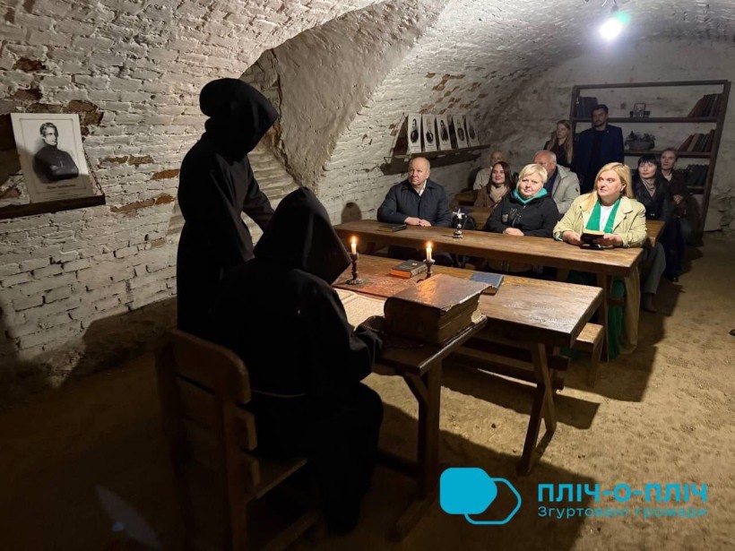 Представники громад у старовинному підвалі, дивляться виставу.