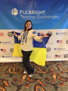 Олена Федорович, учителька історії та права Іллінівського опорного закладу, під час стажування в США на фоні банера проєкту та з українським прапором у руках