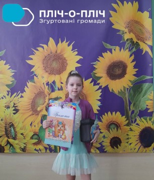Дружківчанка Поліна Гергель тримає грамоту учасниці художнього конкурсу на на фоні банеру,  на якому намальовані соняшники.