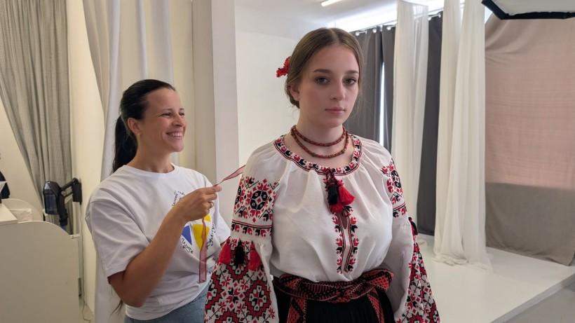 Фотографиня поправляє стрічку у волоссі дівчини, яка вдягнена у традиційну українську вишиванку з червоно-чорним орнаментом