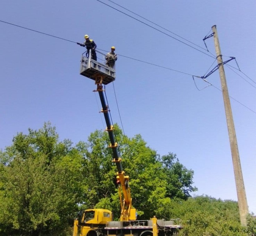 Два співробітники ДТЕК ремонтують електромережі на підйомнику.
