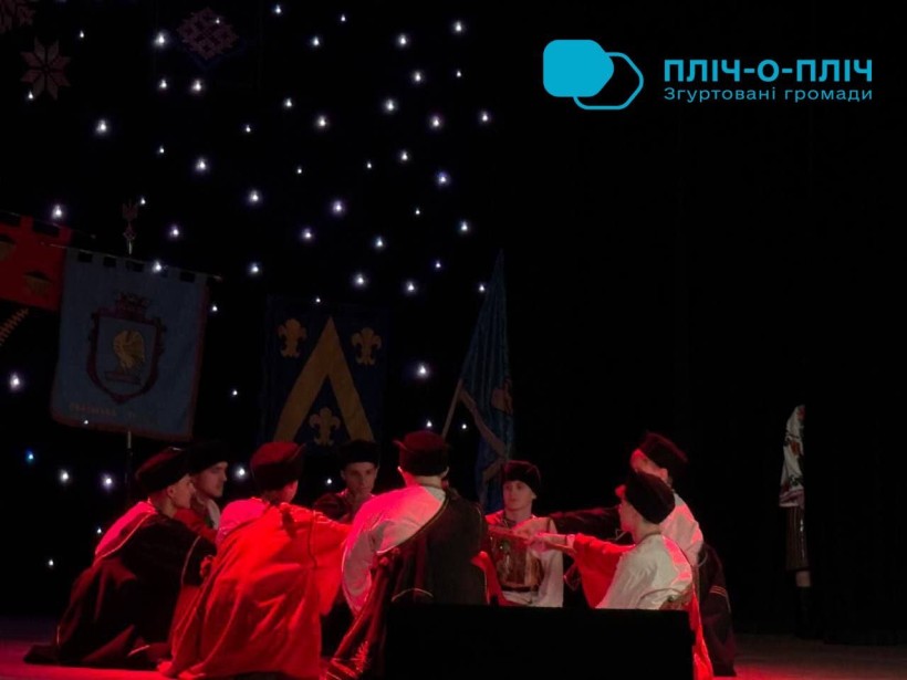 Хлопці у народних костюмах сидять у кругу, дія с музичної вистави.