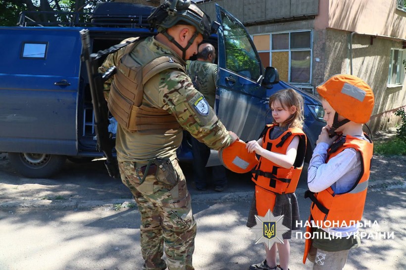 Поліцейський допомагає дитині вдягнути бронежилет та каску