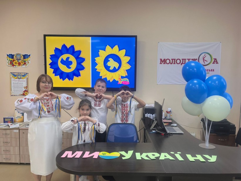 Вчителька та учні у вишиванках складають руками фігуру серця. Поряд напис: "Ми любимо Україну".