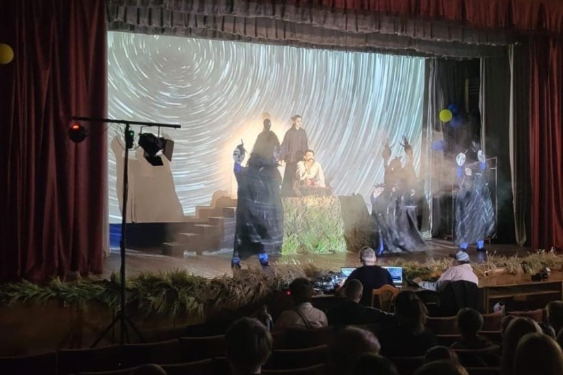 Сцена театру під час вистави з акторами у костюмах та проєкцією зоряного неба на екрані