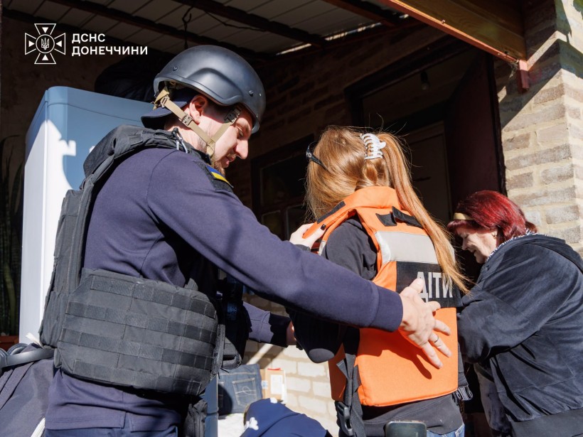 Рятувальник допомагає дівчинці в бронежилеті сісти до евакомобіля