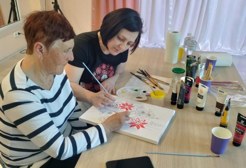 Майстриня допомагає жінці похилого віку розмальовувати полотно з традиційним українським орнаментом під час майстер-класу.