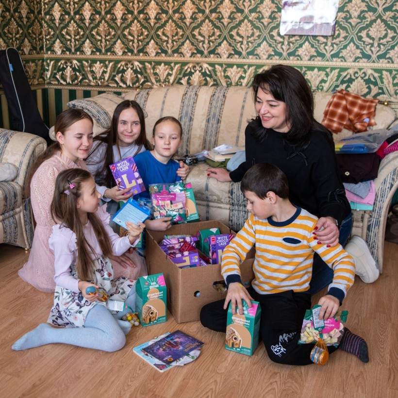 Діти сидять на підлозі та роздивляються подарунки.