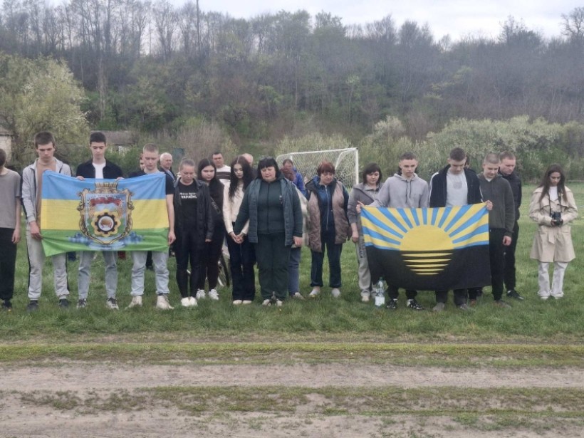 Учасники змагань стоять на футбольному полі та тримають прапори громад.
