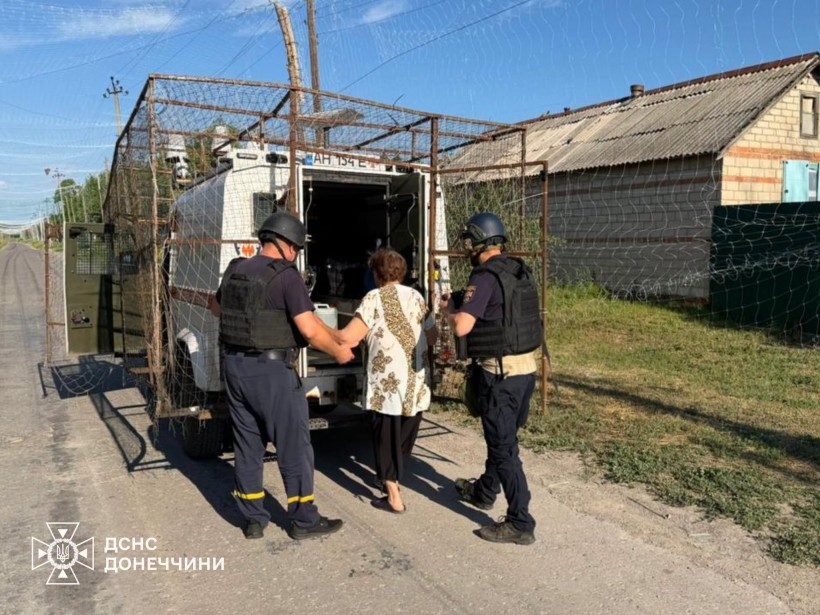 Рятувальники групи "Фенікс" допомагають жінці сісти в евакомобіль