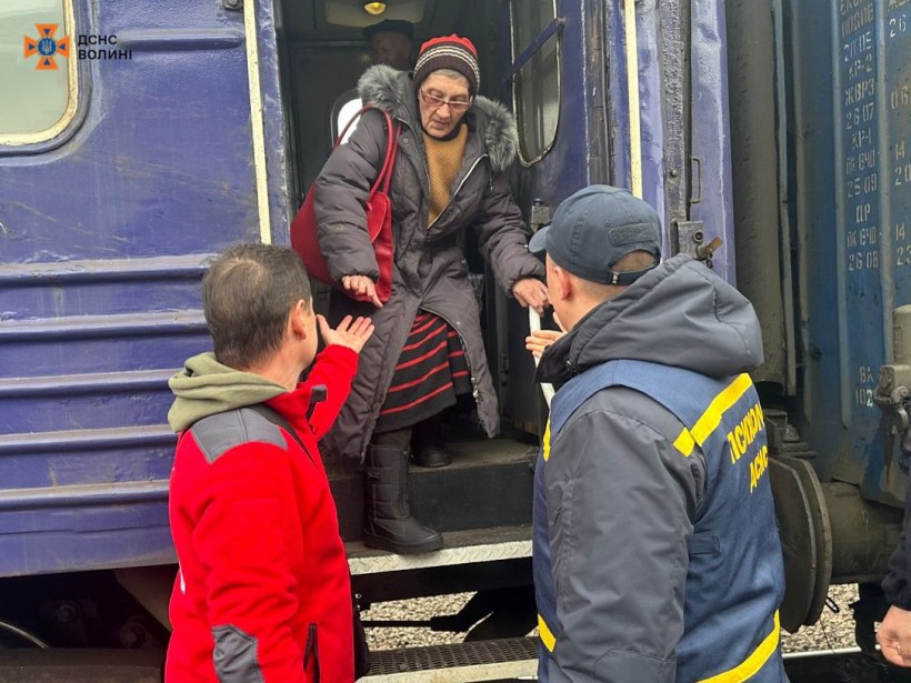 Працівник Червоного Хреста та представник ДСНС допомагають літній жінці вийти з вагона евакуаційного потяга