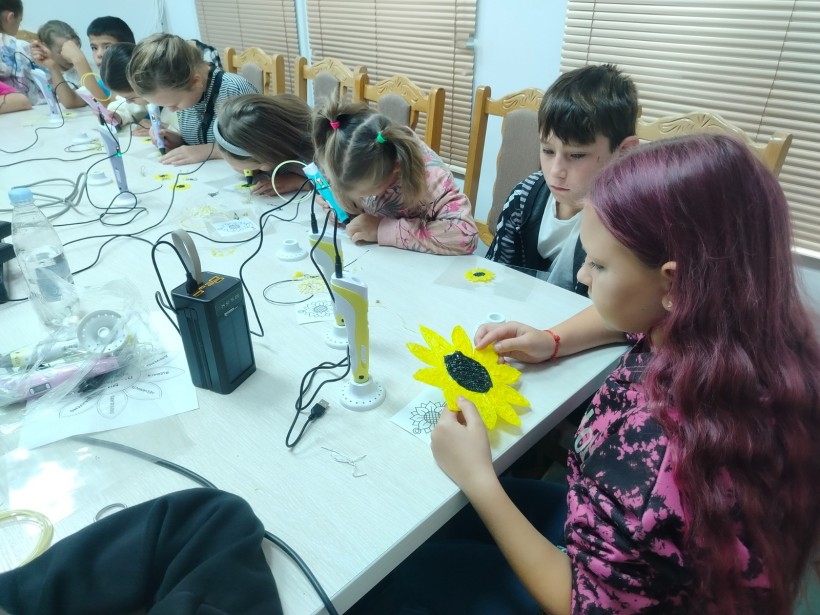Дівчина тримає в руках готову об'ємну фігурку соняшника з жовтими пелюстками та чорною серединкою