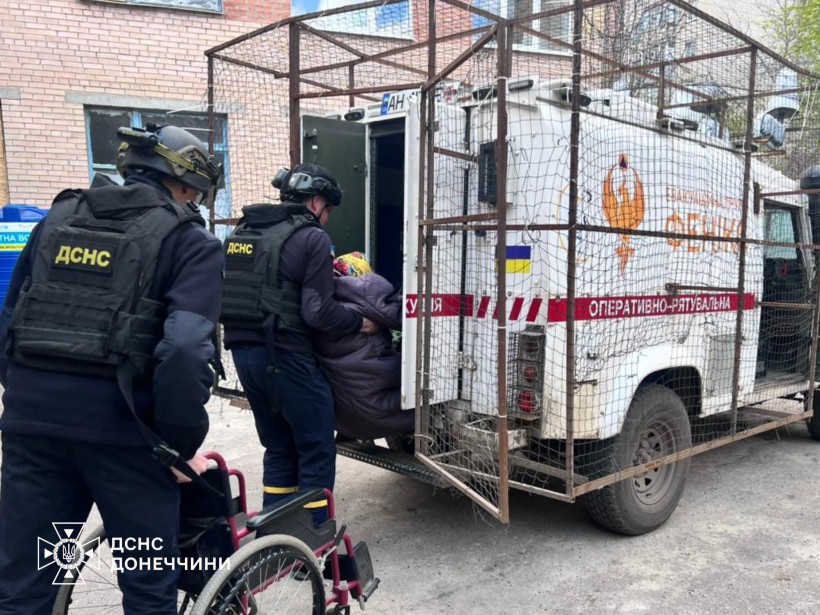 Рятувальники групи "Фенікс" вантажать маломобільну жінку на евакомобіль, поруч її крісло колісне