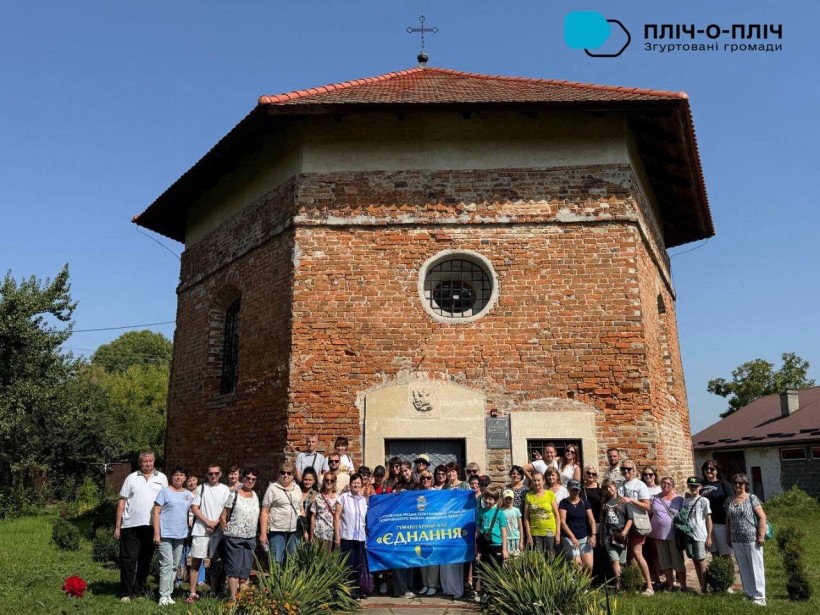 Група переселенців фотографується на фоні старовинної будівлі