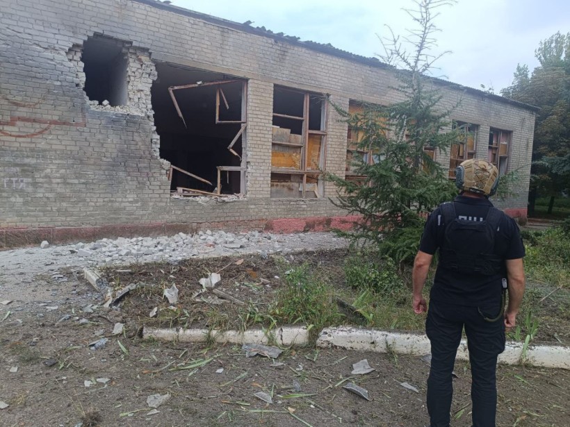 Правоохоронець стоїть поруч зі зруйнованою ворожим обстрілом господарською будівлею