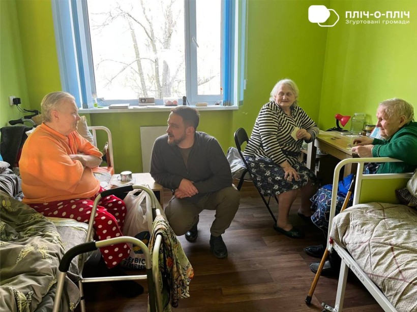 Заступник начальника Часовоярської міської військової адміністрації Руслан Прийменко, сидить поруч з жінками похилого віку, які мешкають в будинку ветеранів.