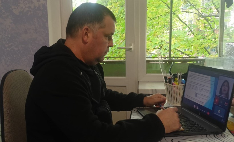 Представник військової адміністрації сидить за столом та слухає доповідача на семінарі