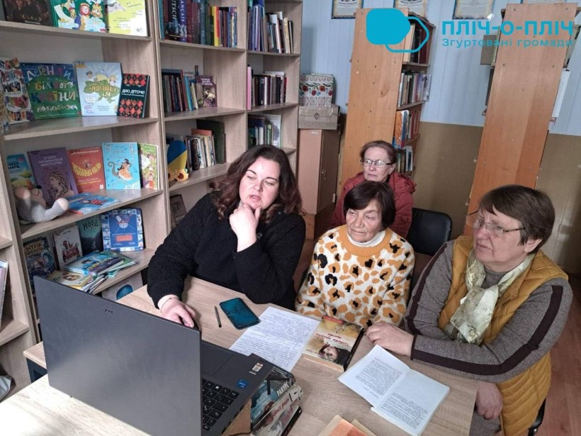 Учасники круглого столу «Тиждень читання: ідеї, що працюють» сидять в бібліотеці перед ноутбуком